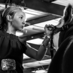 Young girl indoors holding a horse’s reins under a ceiling with metal beams and lights