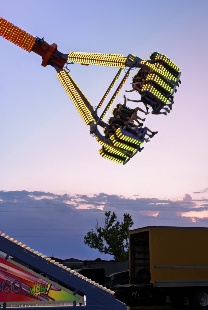 Carnival ride with illuminated seats and riders swinging high against sunset sky.