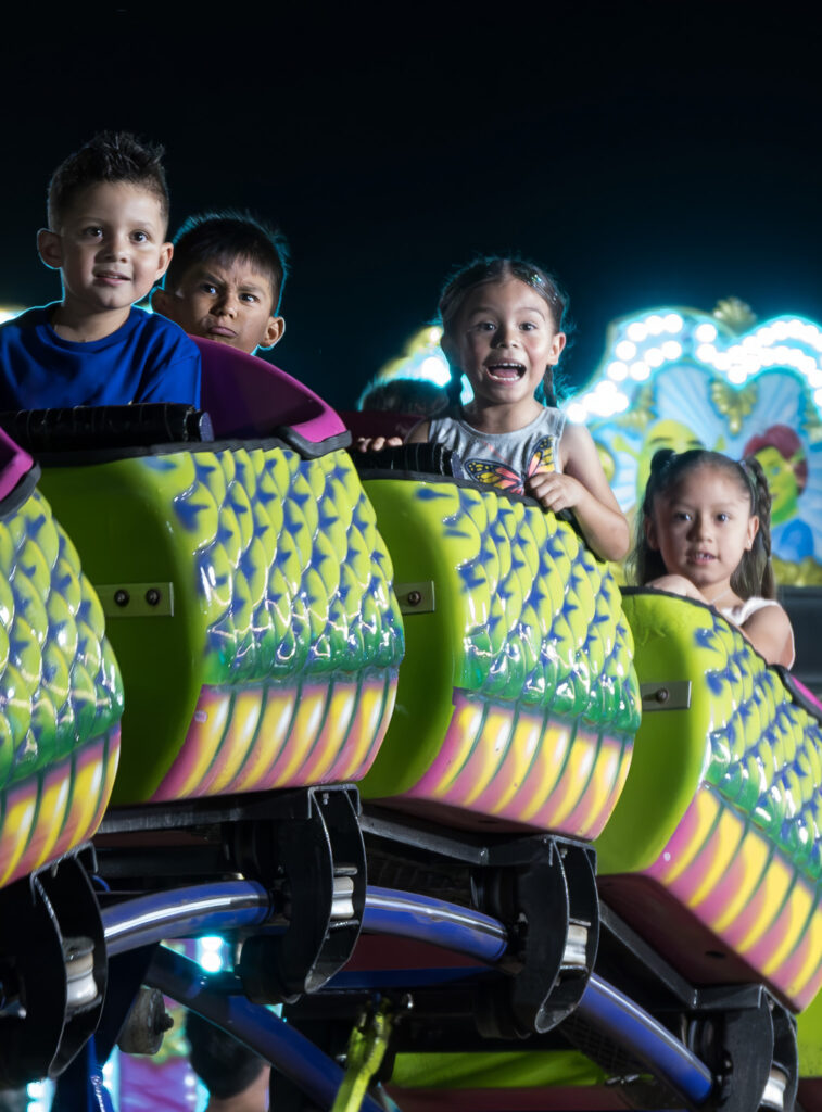 Children riding a colorful amusement park ride at night with illuminated decorations in the background