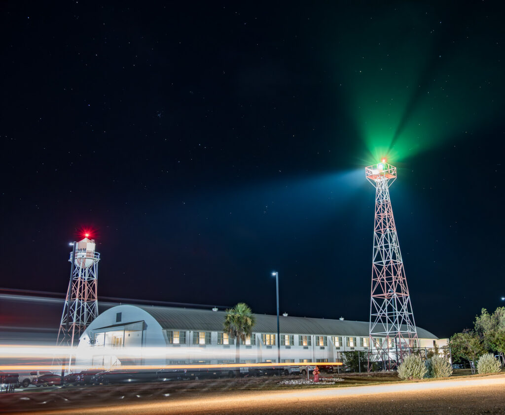 Night scene of a building with two lighted towers emitting red, green, and blue beams with starry sky.
