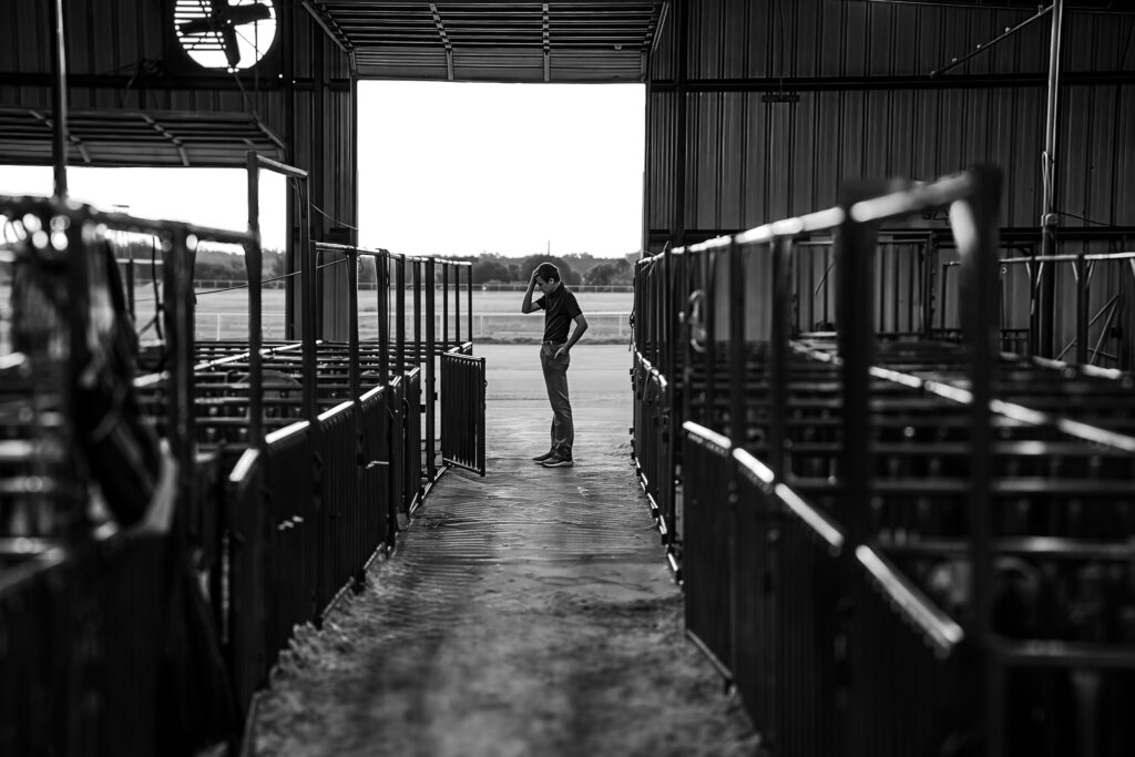 Person stands inside empty stall rows in a large black and white indoor facility with an open entrance.
